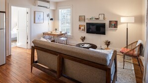A cozy living room with a sofa, a TV, and a dining area with a table and chairs. - Retro Apartment | Furnished Monthly Rental in Belmont (Charlottesville)