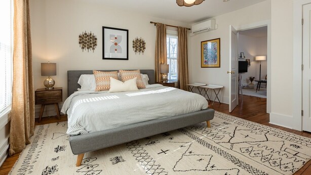 A bedroom with a large bed, a bedside table, a lamp, a rug, and a ceiling light. - Retro Apartment | Furnished Monthly Rental in Belmont (Charlottesville)