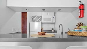 A modern kitchen with white cabinets, a microwave, and a fire extinguisher. - Beachfront by Otium | Pool | Direct Beach Access (San Juan)