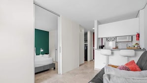A modern hotel room with a bed, a sofa, and a kitchenette area with a microwave and a fire extinguisher. - Beachfront by Otium | Pool | Direct Beach Access (San Juan)