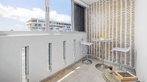 A modern balcony with a large window, a patterned wall, and a small table with a chair. - Beachfront by Otium | Pool | Direct Beach Access (San Juan)