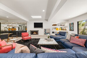 A modern living room with a fireplace, a television, and a dining area with a kitchen in the background.