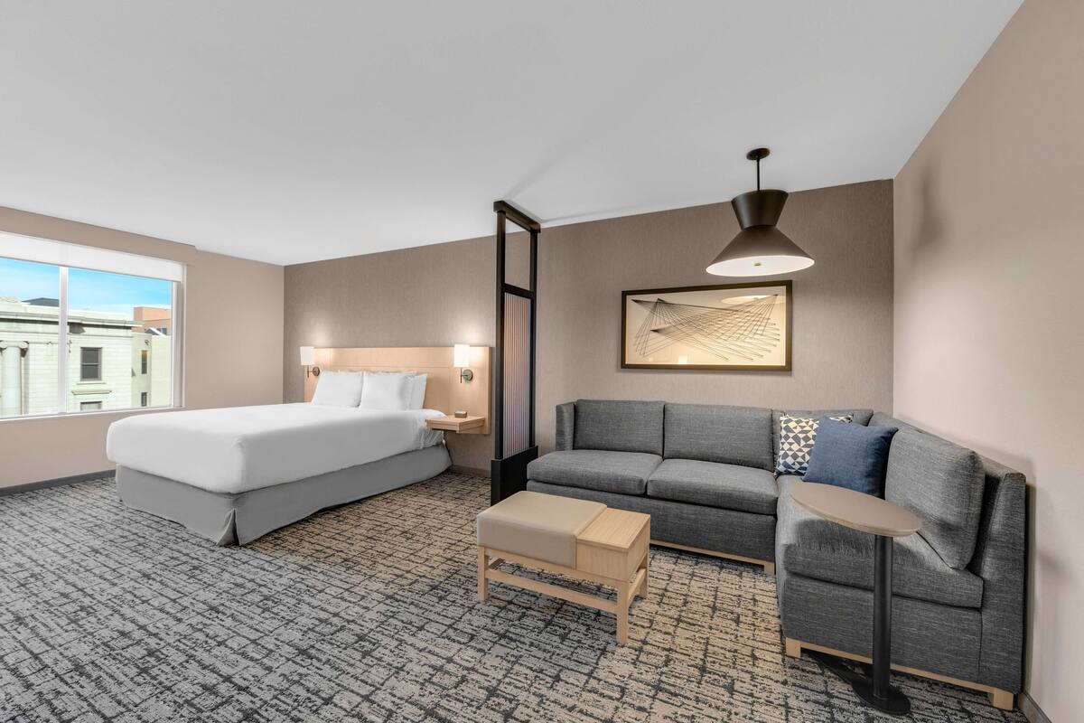 Habitación de hotel con cama, sofá, una mesita y un ventanal grande.