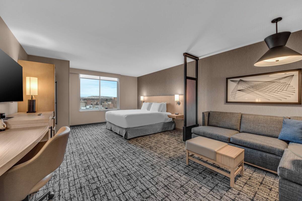 Una habitación de hotel con cama, sofá, escritorio y un ventanal grande.