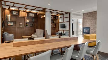 A modern hotel lobby with a long wooden reception desk, grey upholstered seating, a brick accent wall, and a flat-screen TV mounted on the wall.