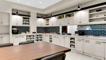 Cozinha moderna com armários brancos, mesa de jantar de madeira e eletrodomésticos em preto e branco.