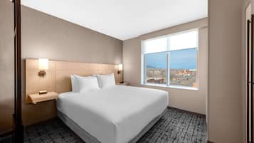 A hotel room with a large bed, two bedside lamps, a nightstand, and a window with a city view.