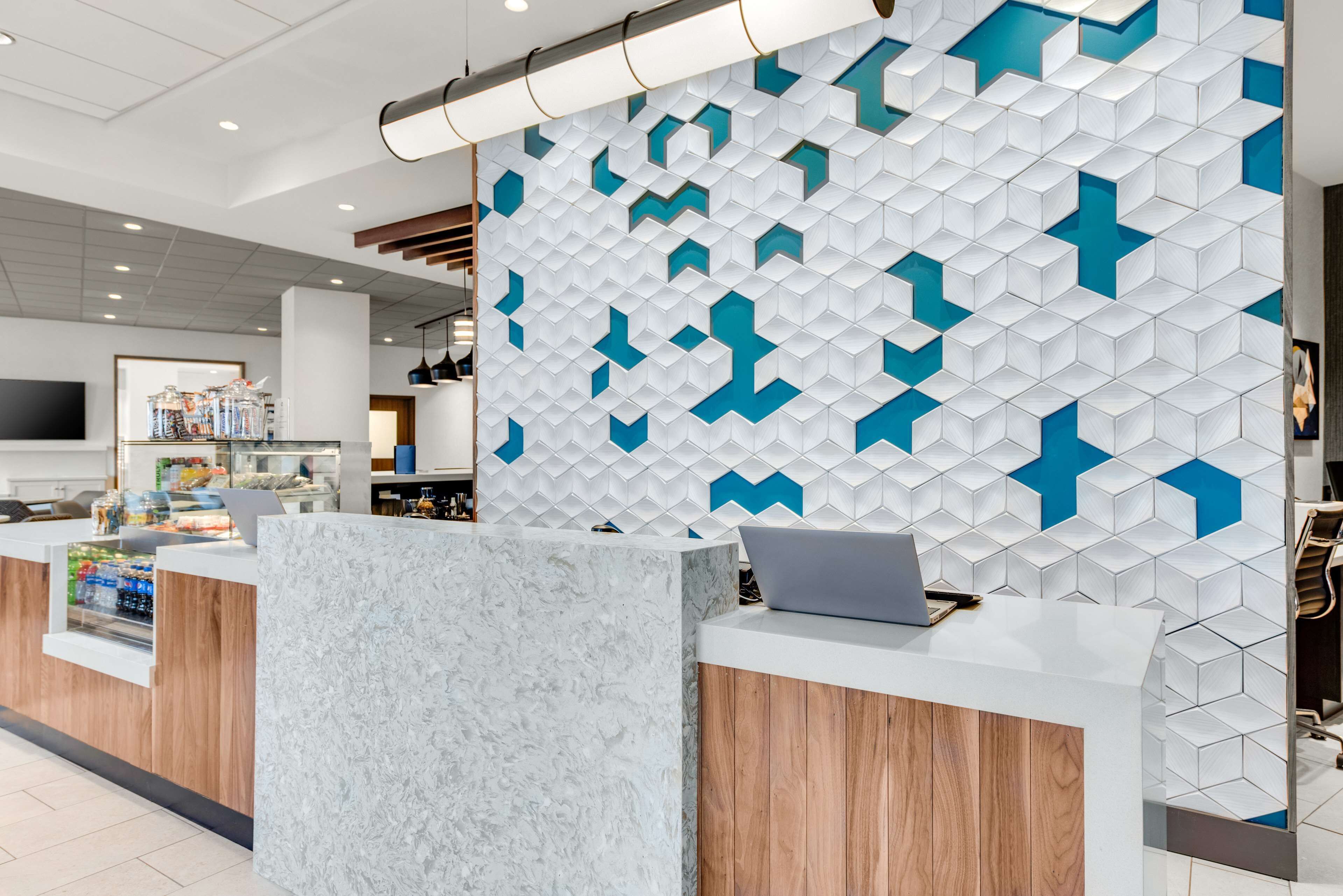 Una moderna zona de recepción con mostrador de mármol, una computadora portátil y una pared con diseño geométrico.