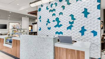 Una moderna zona de recepción con mostrador de mármol, una computadora portátil y una pared con diseño geométrico.
