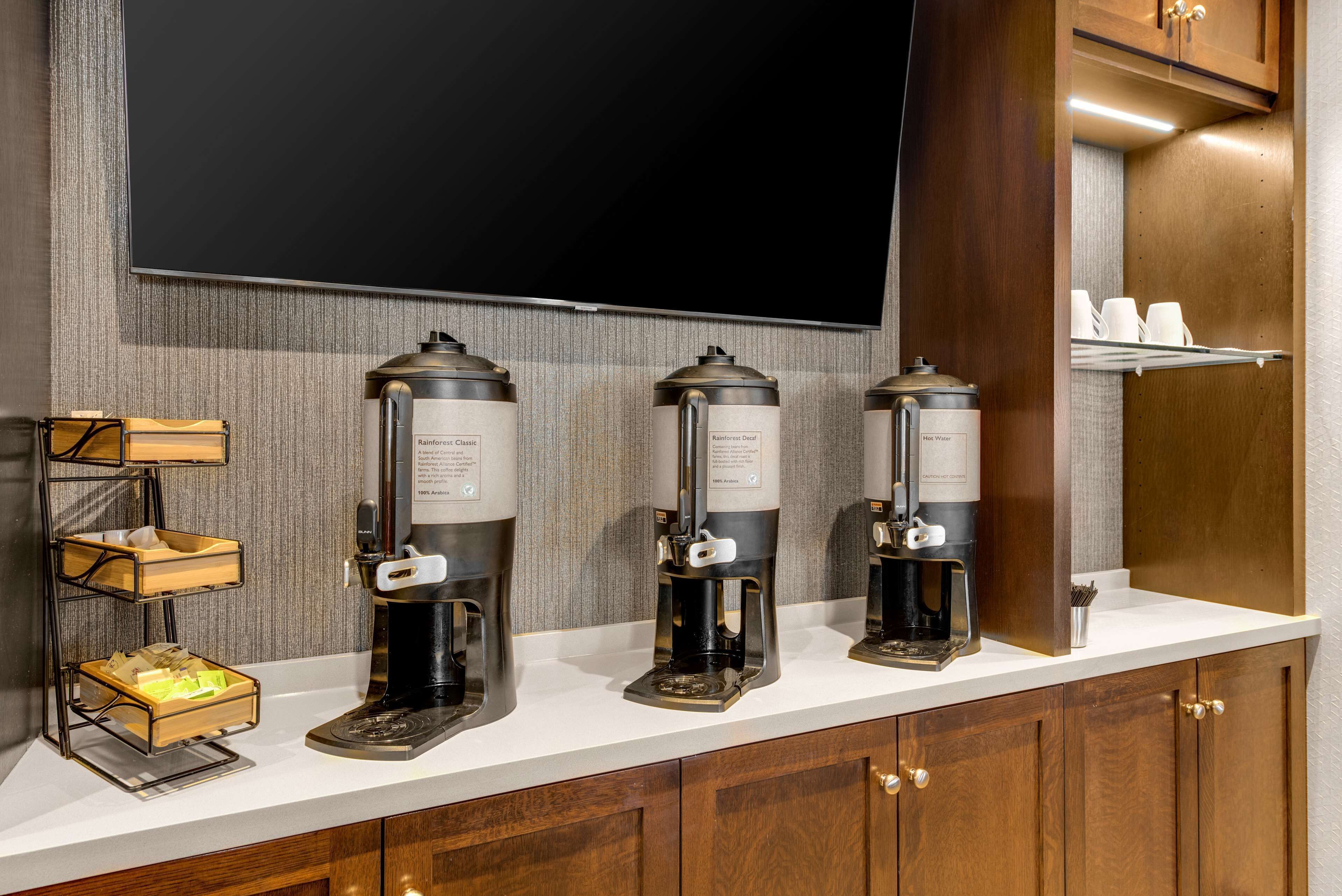 A coffee station with three coffee makers and a tray of cups.