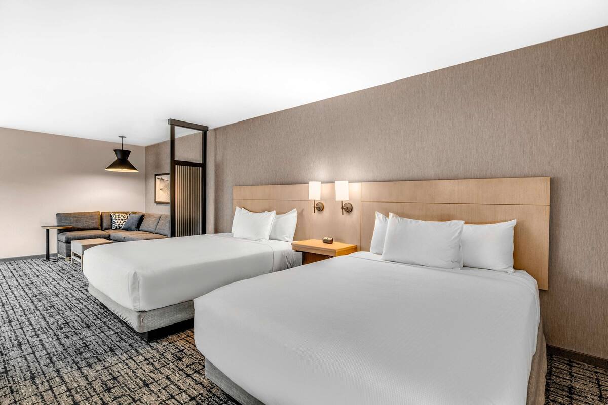 Una habitación de hotel con dos camas, un sofá, una mesita y una lámpara.