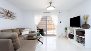 A living room with a sofa, a glass coffee table, a TV, and a bookshelf. - Medano Beach (El Medano)