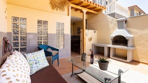 An outdoor patio with a glass table, wicker furniture, and a stone oven. - Medano Beach (El Medano)
