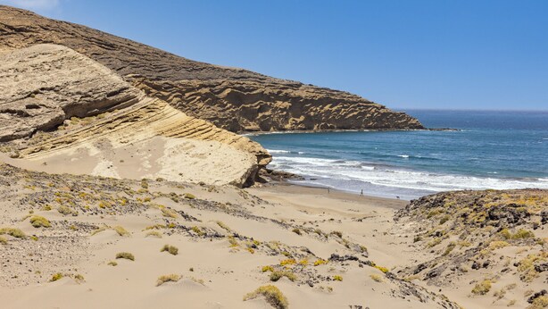 A coastal landscape with a sandy beach, rocky cliffs, and the ocean. - Medano Beach (El Medano)