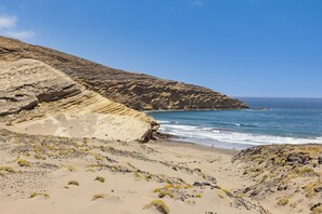 Un paysage côtier avec une plage de sable, des falaises rocheuses et l’océan.