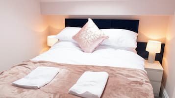 Ein ordentlich bezogenes Bett mit dunklem Kopfteil, zwei Nachttischlampen und einem Fenster darüber.