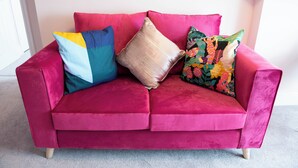 Un canapé en velours rose agrémenté de quatre coussins de différentes couleurs et motifs.
