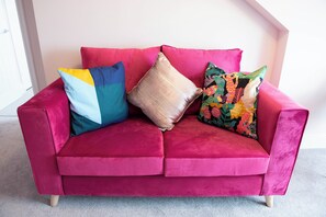Un canapé en velours rose agrémenté de quatre coussins de différentes couleurs et motifs.
