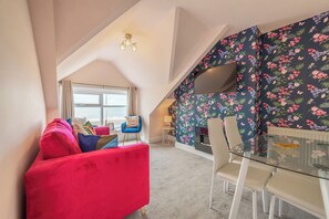 Een gezellige kamer met een rode bank, een glazen tafel en een bloemenbehang.