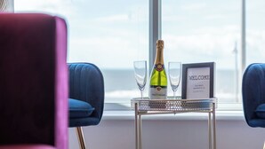 Une pièce avec une table près d’une fenêtre, une bouteille de champagne, deux verres et une pancarte sur laquelle on peut lire « BIENVENUE ».