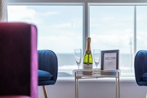 Une pièce avec une table près d’une fenêtre, une bouteille de champagne, deux verres et une pancarte sur laquelle on peut lire « BIENVENUE ».