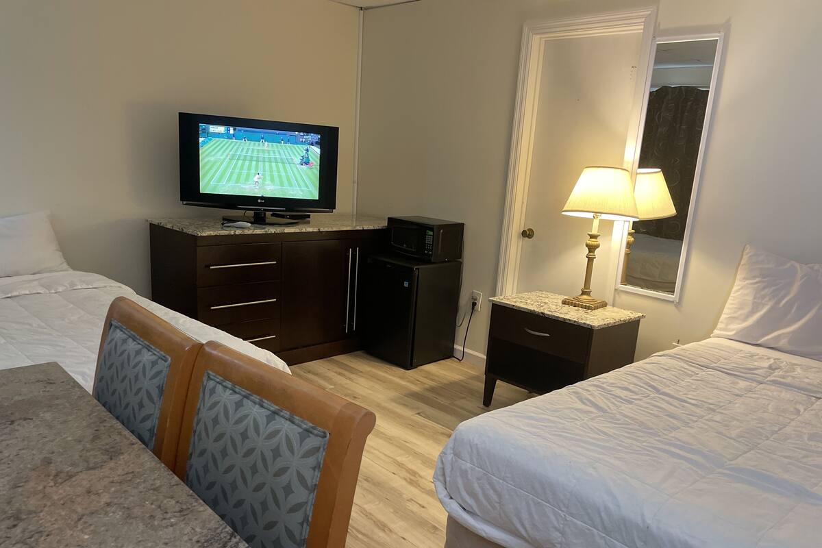 Una habitación de hotel con una cama, un escritorio, un televisor, una lámpara y un armario.