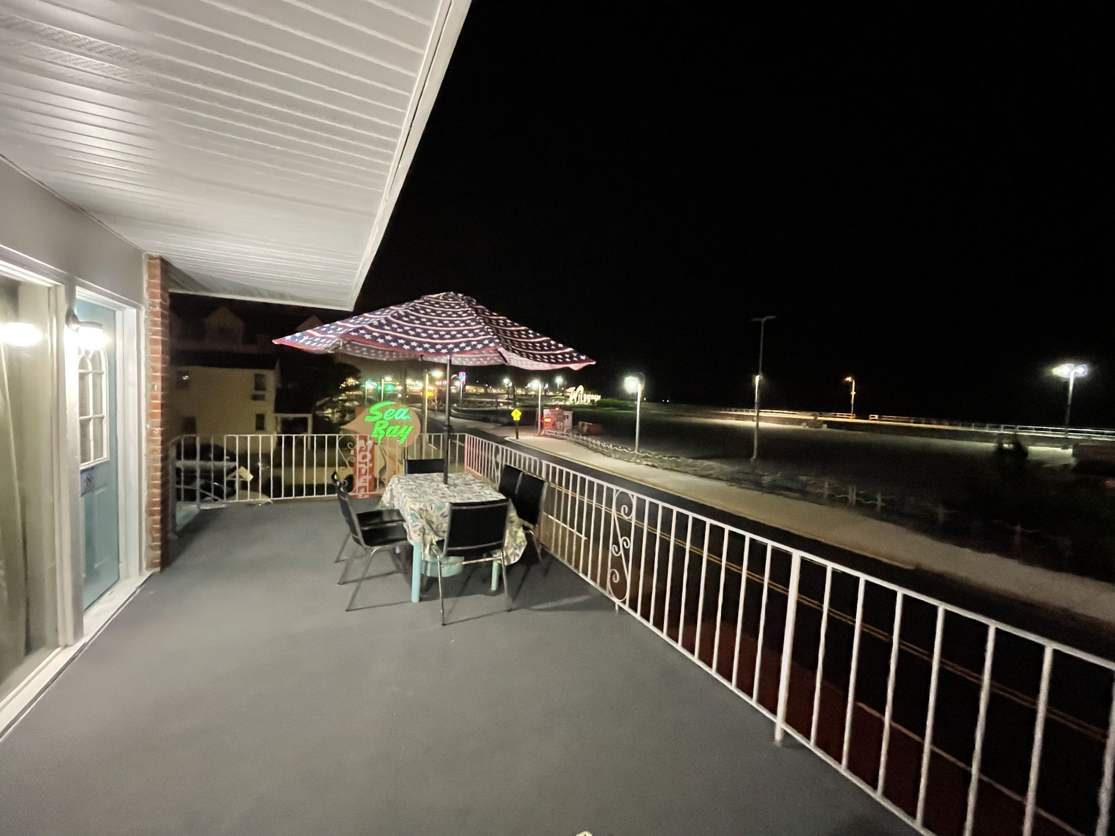 Un balcón con mesa y sillas, un paraguas decorativo y un letrero de neón.