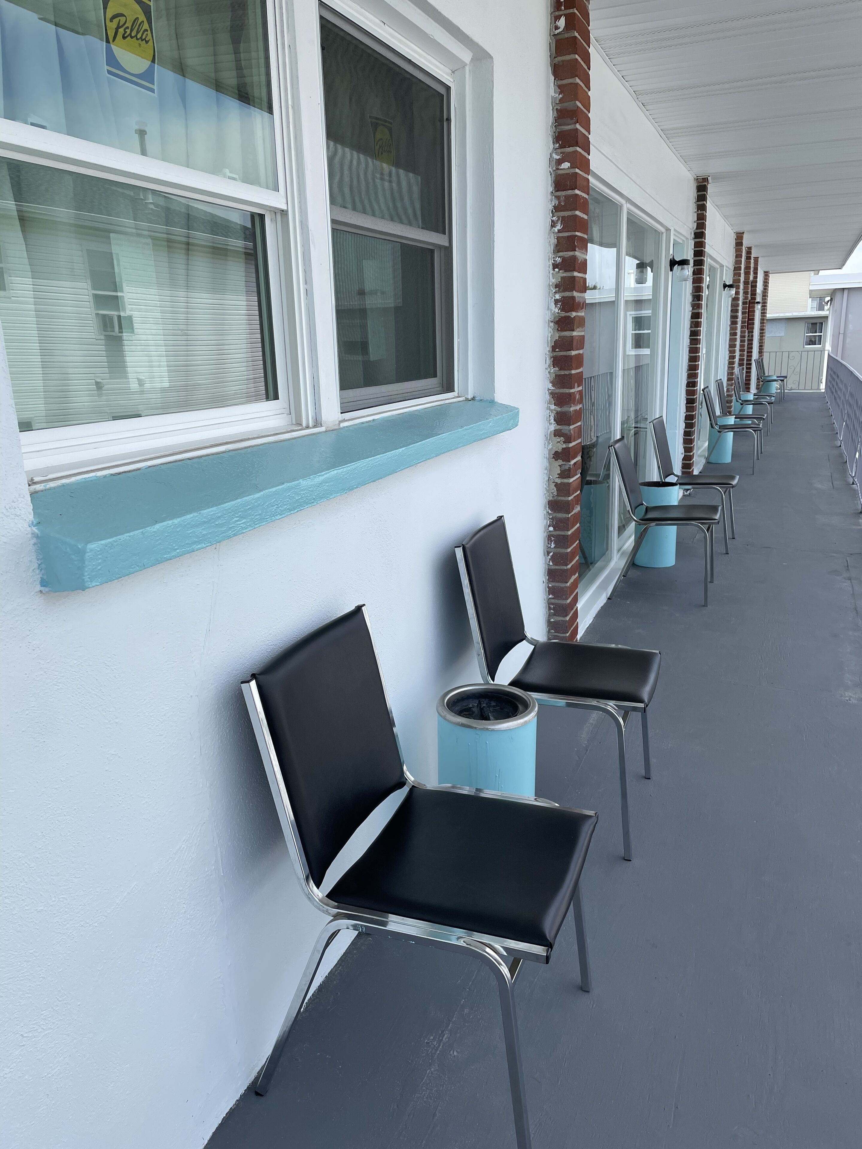 A row of black chairs with metal frames and a light blue painted ledge under the windows of a building.