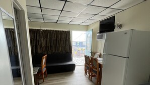A compact kitchen with a refrigerator, a dining table with chairs, and a sofa in the background. - Searay Motel (Wildwood)