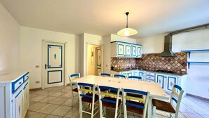 Un coin repas avec une table et des chaises blanches, une cuisine avec des meubles bleus et un sol carrelé.