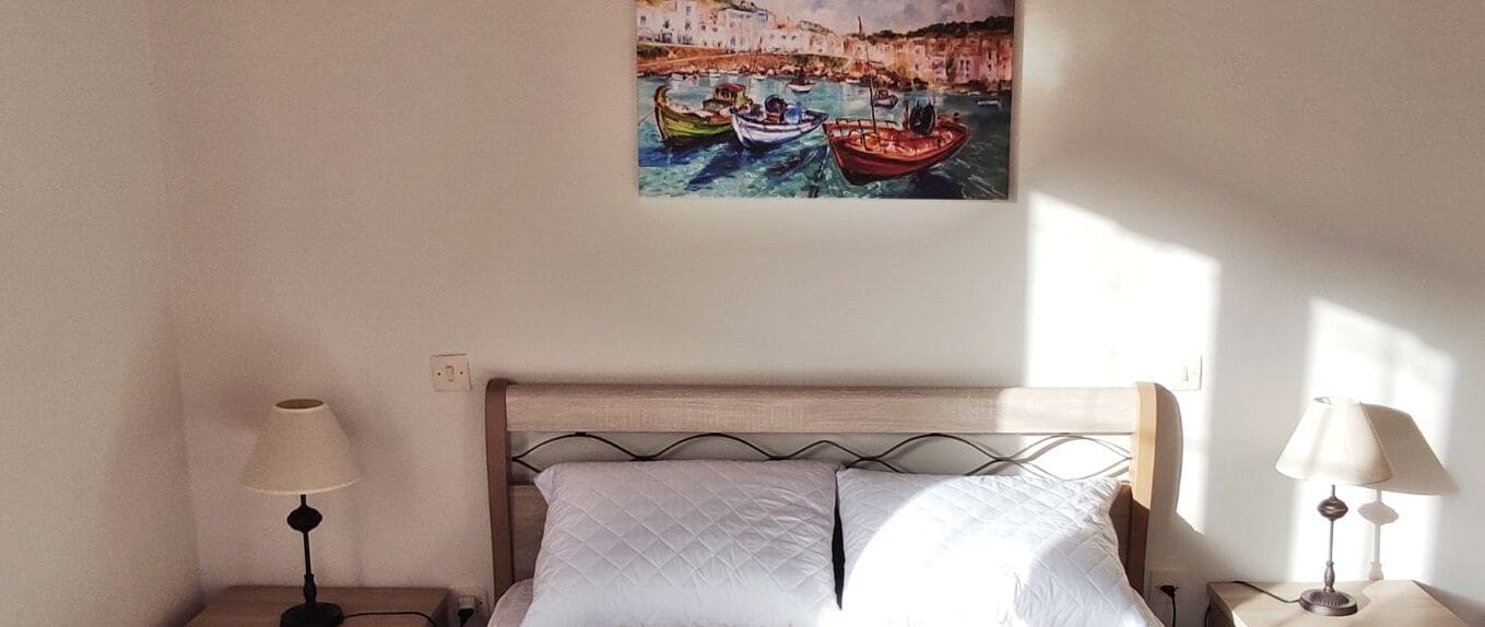 Ein Schlafzimmer mit einem Bett, zwei Nachttischlampen und einem Gemälde von Booten an der Wand.