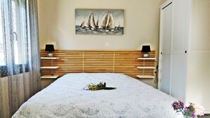 Ein Schlafzimmer mit einem Bett, einem Nachttisch, einer Lampe, einem Bild von Segelbooten und einer Tür.