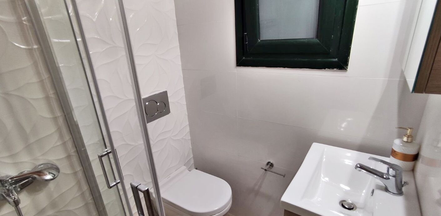 A bathroom with a glass shower enclosure, a white toilet, and a sink with a mirror.