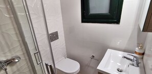 A bathroom with a glass shower enclosure, a white toilet, and a sink with a mirror. - Old Harbour Apartments by CorfuEscapes (Paxos)