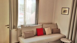 Ein Zimmer mit einem beigefarbenen Sofa, einem kleinen Holzschemel und einem gerahmten Bild an der Wand.