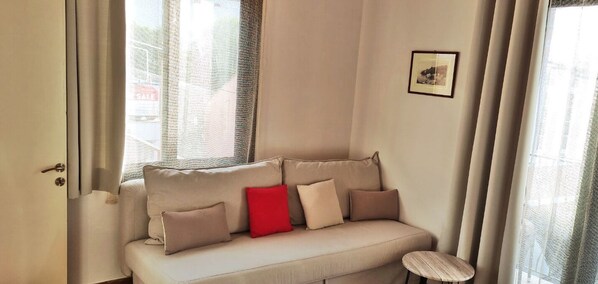 Una habitación con un sofá color beige, un taburete de madera y un cuadro en la pared.