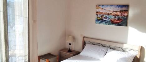 A hotel room with a bed, a nightstand with a lamp, a small table, and a window with curtains.