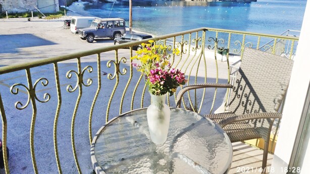 Ein Balkon mit Metallgeländer, ein Tisch mit Blumenvase und Blick auf das Meer sowie ein geparktes Auto.