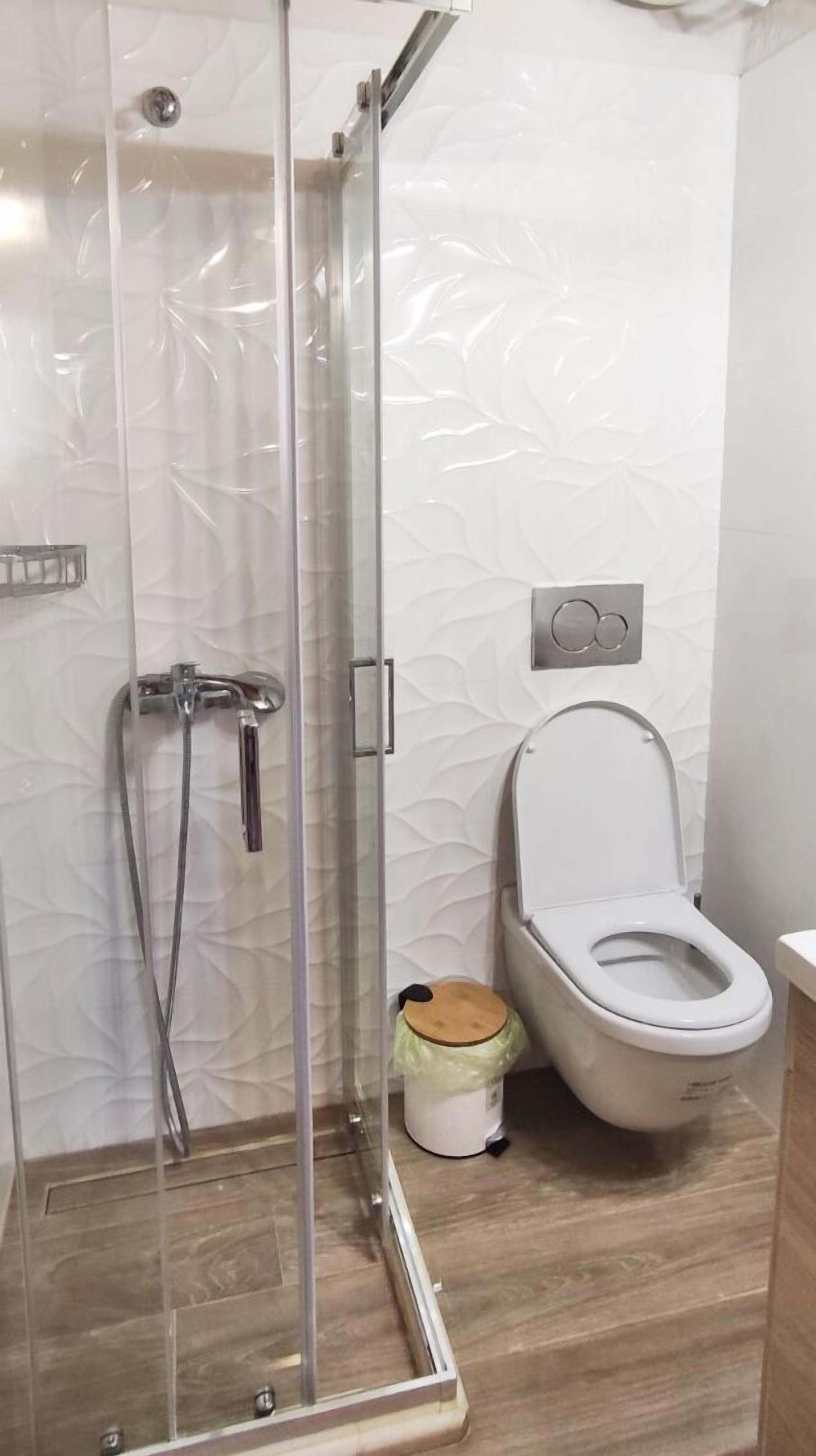 Ein modernes Badezimmer mit Duschkabine aus Glas, Toilette und Mülleimer.