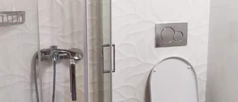 Une salle de bain moderne avec une douche à parois de verre, des toilettes et une poubelle.