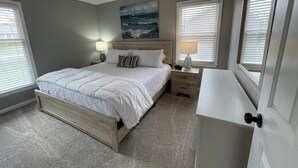 Quarto com cama de madeira, mesa de cabeceira com abajur, quadro na parede e janela com persianas.