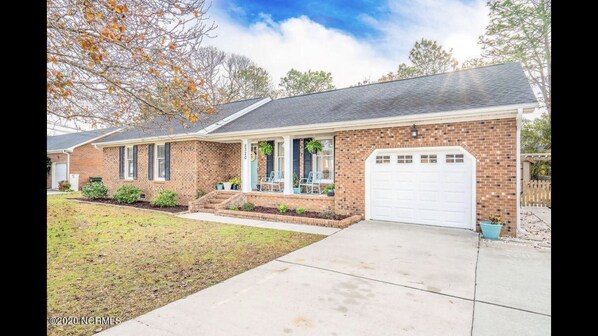 A single-story brick house with a front porch, a garage, and a well-maintained lawn.