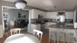 Uma cozinha moderna com armários brancos, uma geladeira de aço inoxidável e uma área de jantar com mesa e cadeiras brancas.