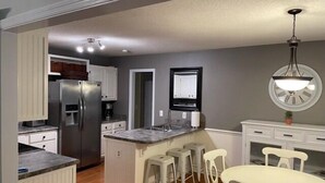 Uma cozinha compacta com ilha central, armários brancos e um espaço de refeições com cadeiras.