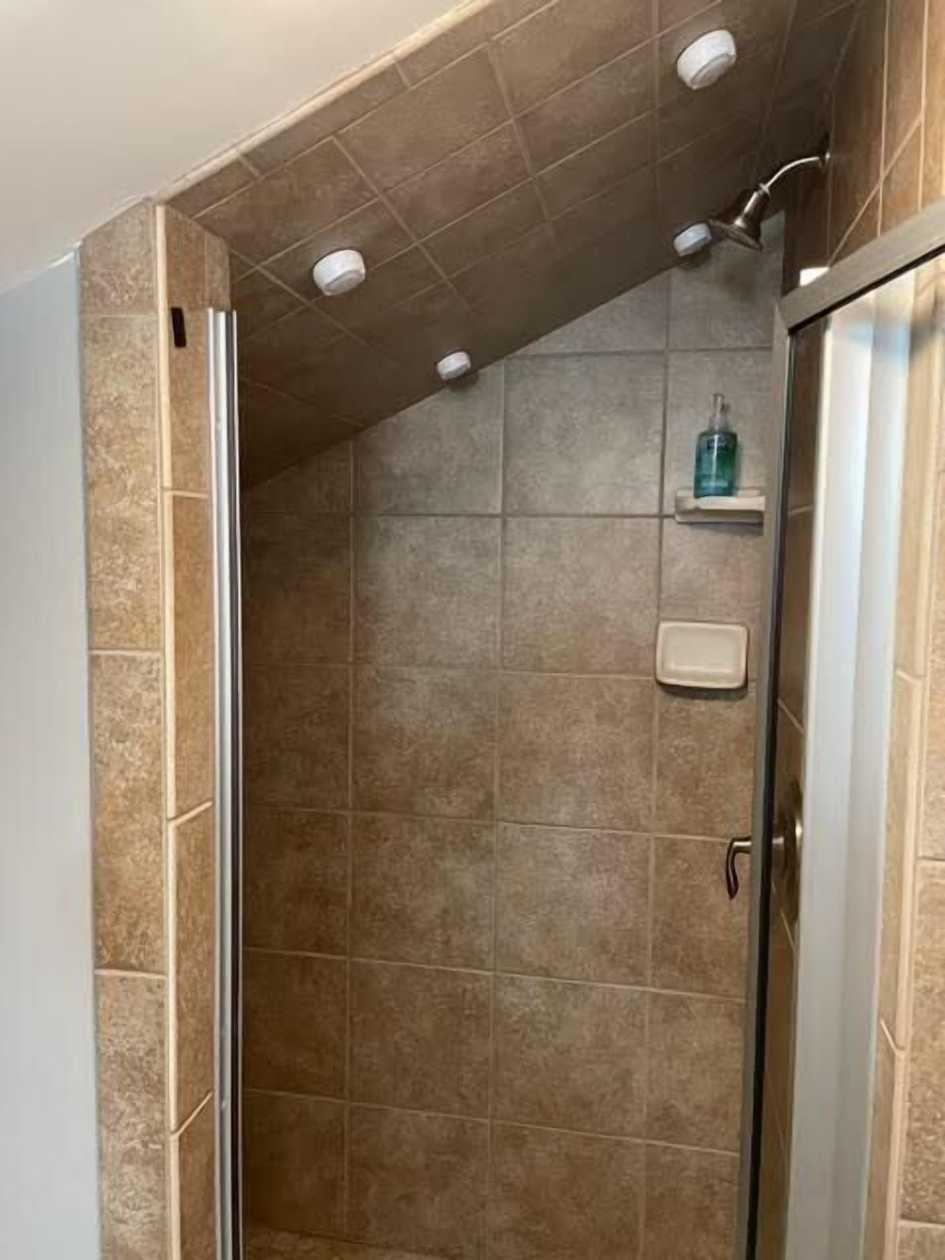 Eine Dusche mit beigen Fliesen, einer Glastür und einem Seifenspender an der Wand.