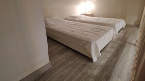 A room with two single beds, a nightstand with a lamp, and a wooden floor. - Agréable Studio Dans Jardin Paysager Avec Piscine et Grande Cuisine D'été (Bagnols-en-Forêt)