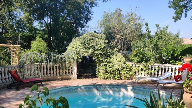 A swimming pool surrounded by a stone balustrade, with two lounge chairs and a wooden pergola in the background. - Agréable Studio Dans Jardin Paysager Avec Piscine et Grande Cuisine D'été (Bagnols-en-Forêt)
