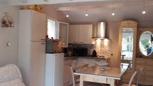 A compact kitchen with a dining area, featuring a refrigerator, microwave, and tiled backsplash. - Agréable Studio Dans Jardin Paysager Avec Piscine et Grande Cuisine D'été (Bagnols-en-Forêt)