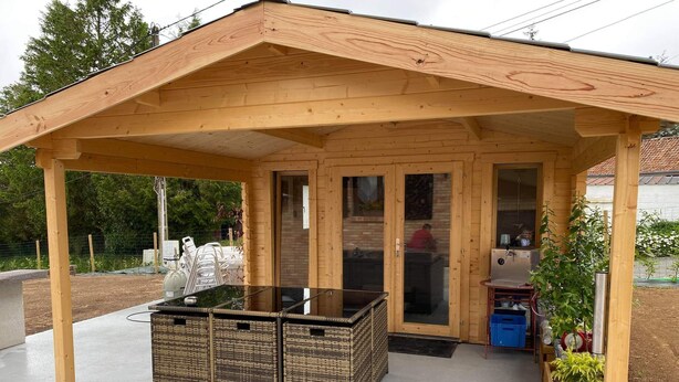A wooden pavilion with a glass door, a concrete floor, wicker furniture, and a small garden area. - Gîte "prima Luce" (Preures)