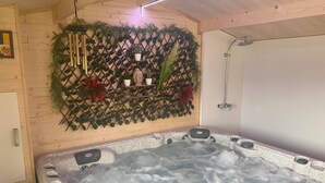 A spa room with a hot tub, wooden walls, and a decorative wall with plants and a Buddha statue. - Gîte "prima Luce" (Preures)